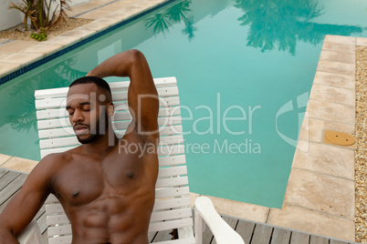 Man relaxing with eyes closed on a sun lounger near swimming pool at the backyard of home