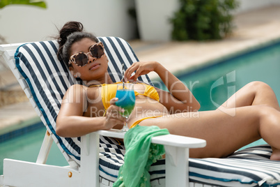 Woman in bikini relaxing on a sun lounger near swimming pool at the backyard of home