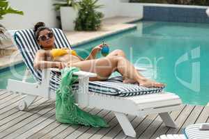 Woman in bikini relaxing on a sun lounger near swimming pool at the backyard of home