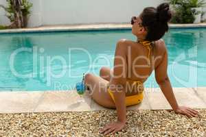 Woman in bikini relaxing at the edge of swimming pool in the backyard