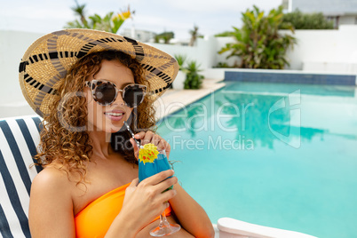 Woman having cocktail drink while relaxing on a sun lounger in the backyard of home