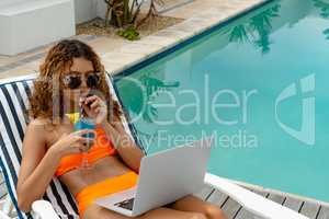 Woman using laptop while having cocktail drink in the backyard at home