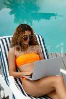 Woman using laptop while relaxing on a sun lounger in the backyard at home