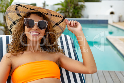 Woman in bikini relaxing on a sun lounger near swimming pool at the backyard of home