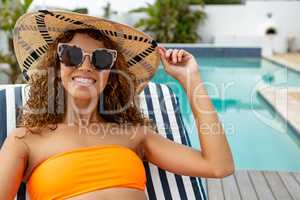 Woman in bikini relaxing on a sun lounger near swimming pool at the backyard of home