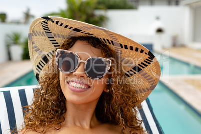 Happy woman relaxing on a sun lounger near swimming pool at the backyard of home