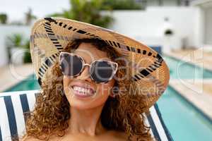 Happy woman relaxing on a sun lounger near swimming pool at the backyard of home