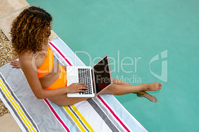 Woman using laptop while sitting at the edge of swimming pool