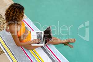 Woman using laptop while sitting at the edge of swimming pool