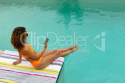 Woman using mobile phone while sitting at the edge of swimming pool