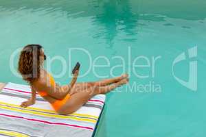 Woman using mobile phone while sitting at the edge of swimming pool