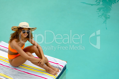Woman in sunglasses and hat sitting at the edge of swimming pool