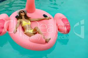 Woman in bikini relaxing on a inflatable tube in swimming pool at the backyard of home