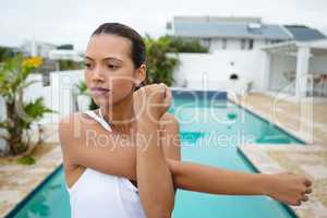 Fit woman performing stretching exercise near swimming pool in the backyard