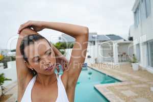 Fit woman performing stretching exercise near swimming pool in the backyardw