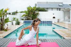 Woman performing stretching exercise near swimming pool in the backyard