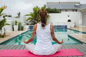 Fit woman performing yoga near swimming pool in the backyard