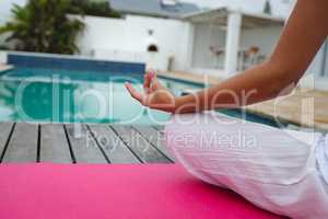 Woman performing yoga near swimming pool in the backyard