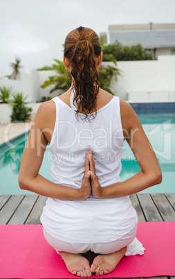 Woman performing yoga near swimming pool in the backyard