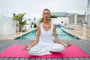 Woman performing yoga near swimming pool in the backyard