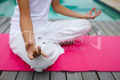 Woman performing yoga near swimming pool in the backyard