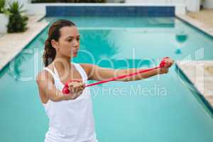 Woman exercising with resistance band near swimming pool in the backyard