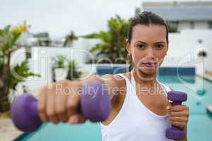Woman exercising with dumbbells near swimming pool in the backyard