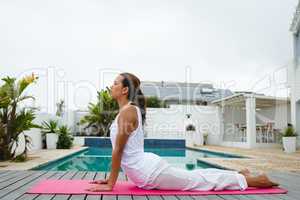 Woman performing yoga near swimming pool in the backyard