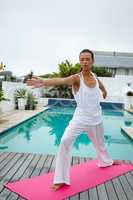 Woman performing stretching exercise near swimming pool in the backyard