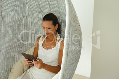 Beautiful woman using digital tablet in comfortable hanging chair