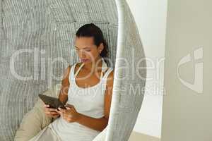 Beautiful woman using digital tablet in comfortable hanging chair