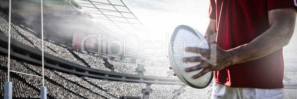 Composite image of rugby player holding football at field.