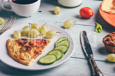 Slice of frittata with cup of coffee, grapes and muffins.