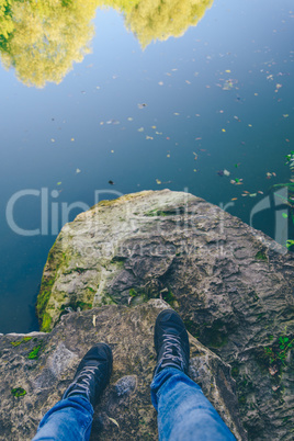 Men's legs stand on a stone in front of the lake.
