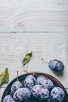 Plums on plate over wooden surface