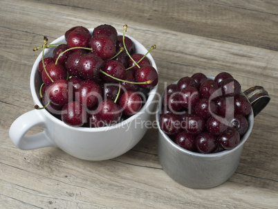 Fresh ripe cherries in cups, on wooden background.