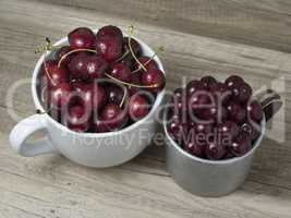 Fresh ripe cherries in cups, on wooden background.