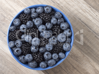 Bowl full of fresh blackberries and blueberries on a wooden back