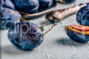 Plums with leaves and knife over wooden surface