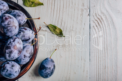 Plums on plate over wooden surface