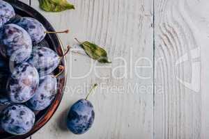 Plums on plate over wooden surface