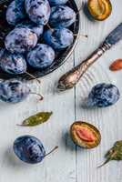 Plums with leaves and knife over wooden surface