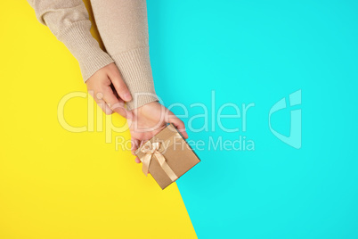 two hands hold a paper closed golden box on a yellow blue backgr