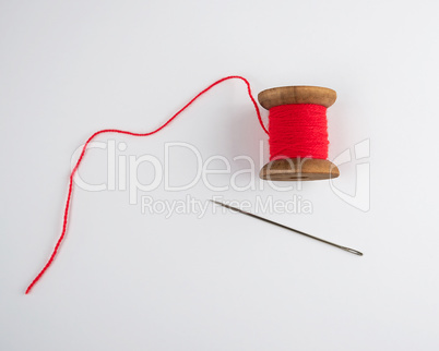 wooden reel with red wool thread and a large needle