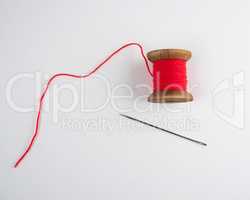 wooden reel with red wool thread and a large needle