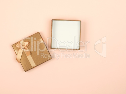 open golden square gift box with a bow on a beige background