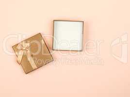 open golden square gift box with a bow on a beige background