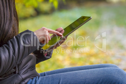 Teenage girl using digital tablet computer in autumn park