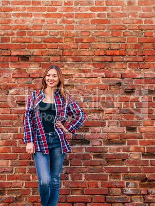 Portrait of young woman standing against brick wall