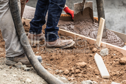 Construction Workers Pouring And Leveling Wet Cement Into Wood